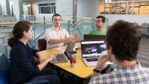 Group of researchers discuss at a table with laptops in front of them.