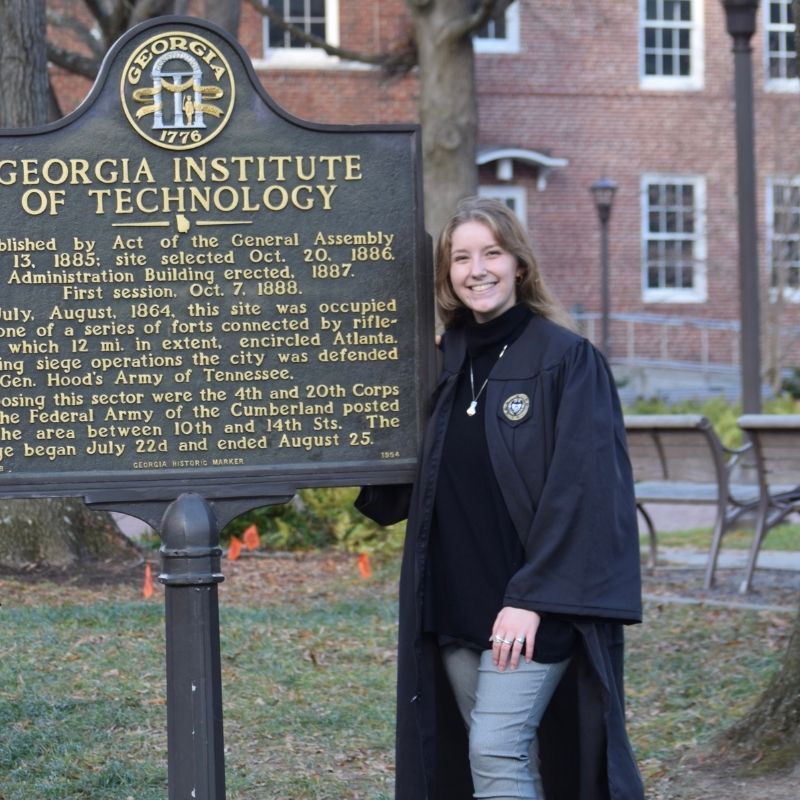 Headshot of Lucy Grant in graduation regalia with the Georgia Tech incorporation sign.