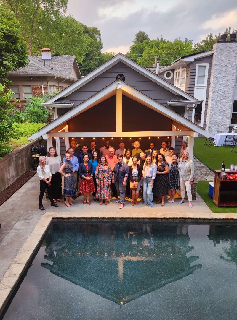 Group of people standing in front of a house and a pool in a backyard