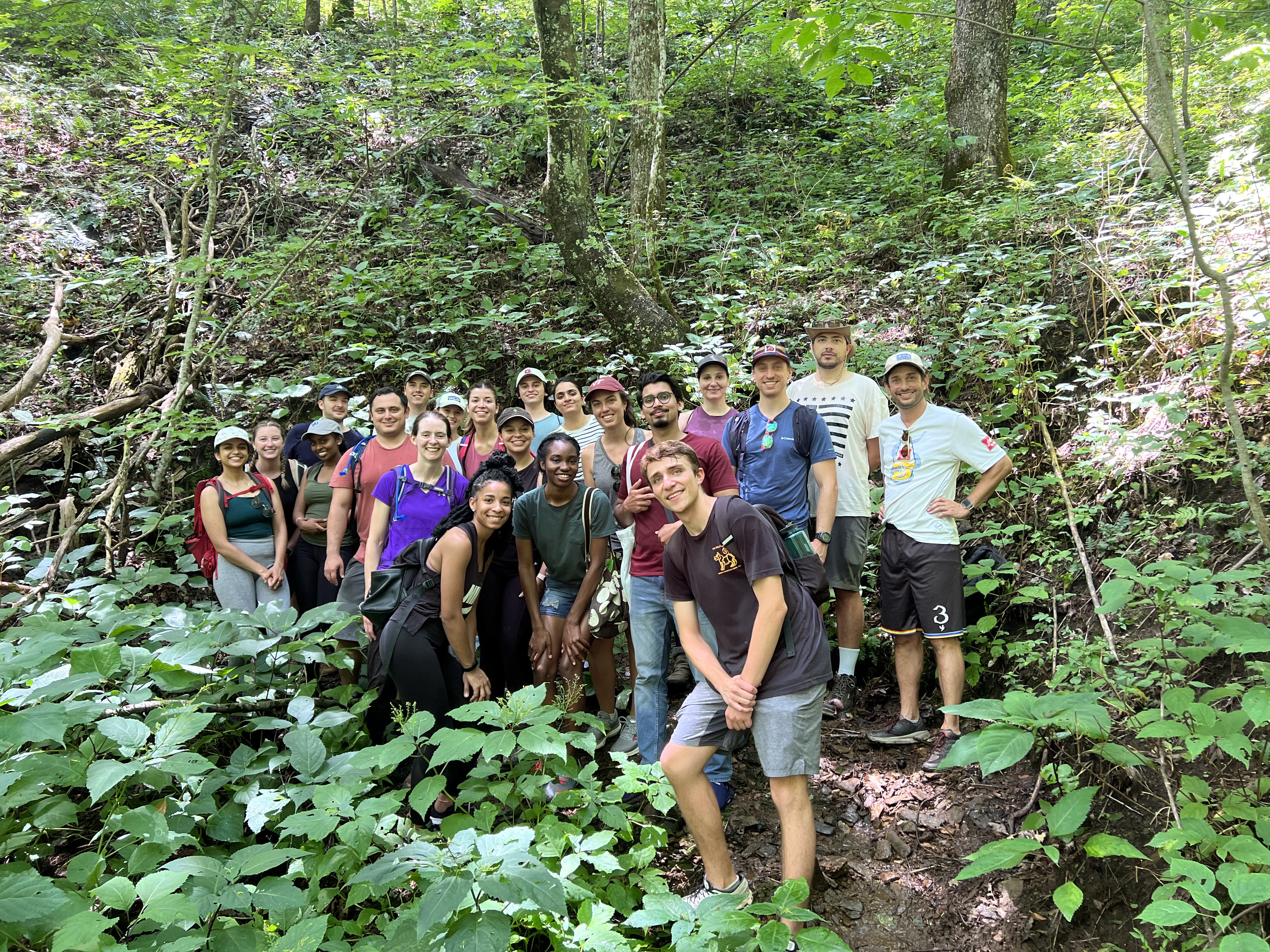 Group of sudents and alumni and Dr. Matisoff standing outdoors surrounded by green leaves and trees.