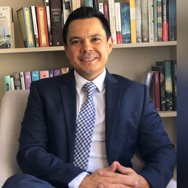 Headshot of Marco Otoya in front of a bookshelf.