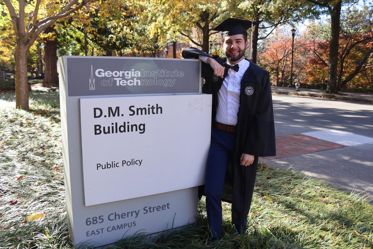 Andrew McGraw poses in graduation regalia outside the DM Smith building.