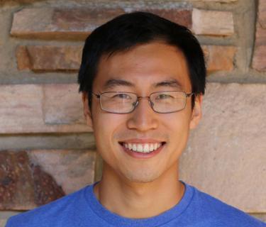 Headshot of Sam Zhang against a wall with spaced out brick.